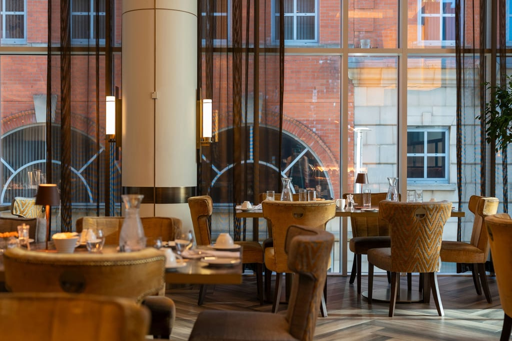 Restaurant dining room in warm light, with red-brick buildings beyond the windows